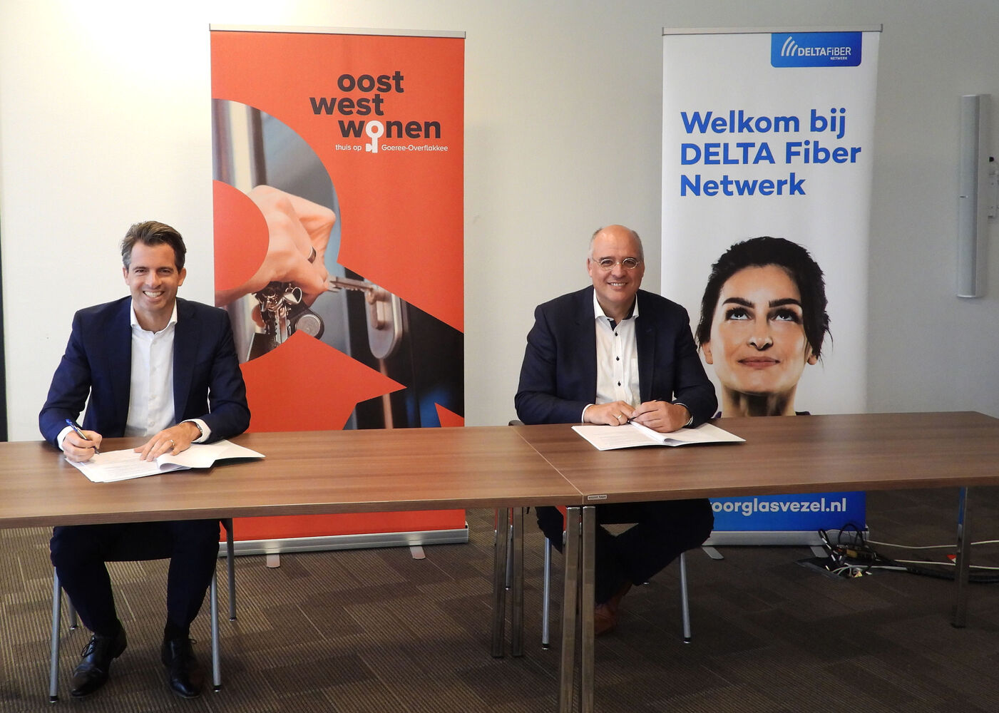Op het beeld zijn Kees van Dam, manager vastgoed bij Oost West Wonen en Michiel Admiraal, directielid DELTA Fiber Netwerk te zien terwijl zij een overeenkomst ondertekenen.