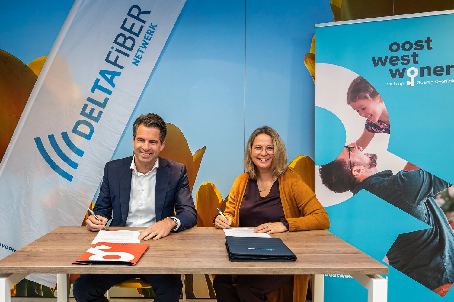 Op het beeld zijn Michiel Admiraal (DELTA Fiber) en Marleen van de Kamp (Oost West Wonen) te zien terwijl zij de overeenkomst ondertekenen.