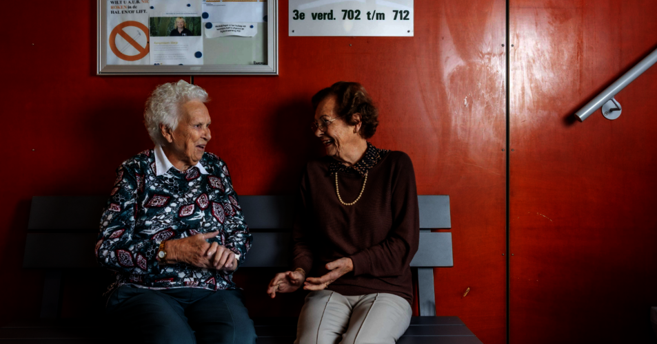 2 dames kletsen op een bankje in de galerij van hun flat