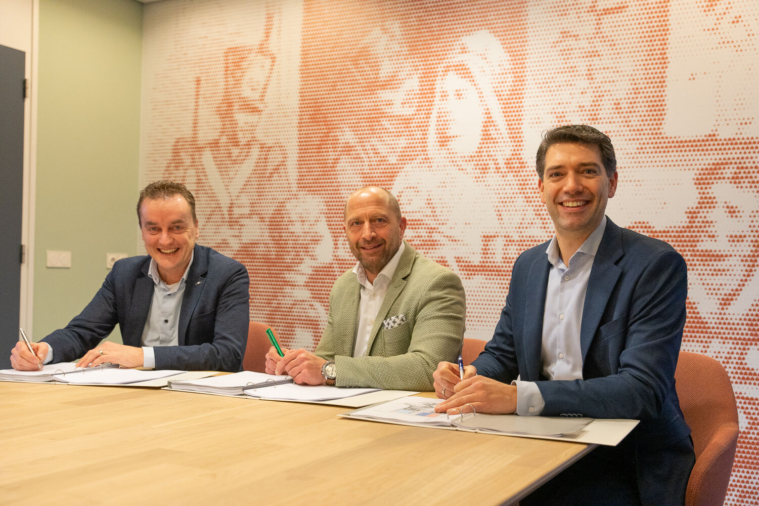 Drie personen zitten aan tafel met documenten en pennen