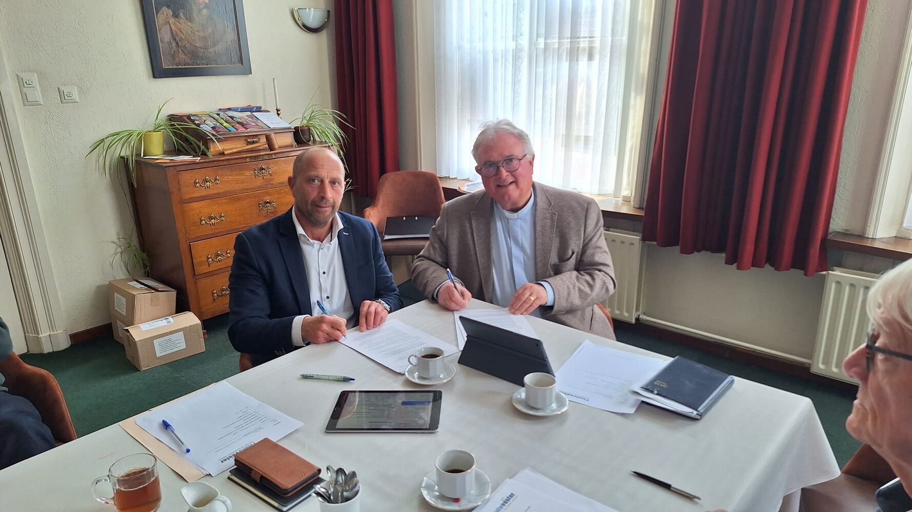 Groep mensen zit aan tafel met documenten en koffie in vergaderruimte