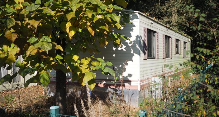 Stacaravan in een groene omgeving met bomen en struiken, gefotografeerd vanaf de zijkant.