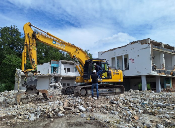 Gele graafmachine op een sloopterrein met puin en deels afgebroken gebouw