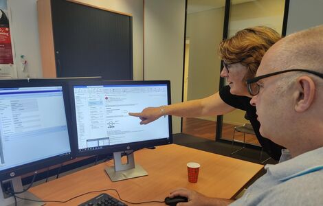 Twee medewerkers van WoonInvest kijken samen naar een computerscherm.
