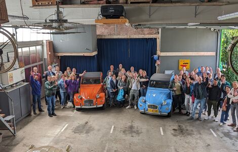 Medewerkers tijdens een bedrijfsuitje in een hal vol met Citroén 2CV's.